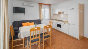 Een knus woongedeelte met een bank, eettafel, stoelen, een televisie, kitchenette en een raam met gordijnen.