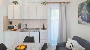 Une cuisine compacte Ă©quipĂ©e dâun four Ă micro-ondes, dâune cuisiniĂšre, dâun Ă©vier et de placards. On y trouve une table Ă manger avec des fruits et un canapĂ© avec des coussins.