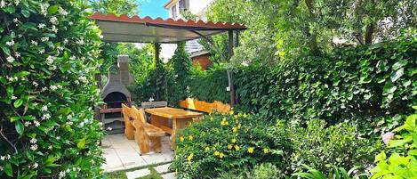 A garden patio with a stone table and chairs, a brick oven, and a pergola.