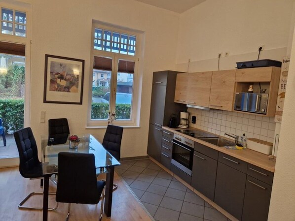 A modern kitchen with a dining table and chairs, a refrigerator, oven, and a coffee maker. - (22) 2-room apartment - apartment house Sonnenresidenz I (Kühlungsborn)