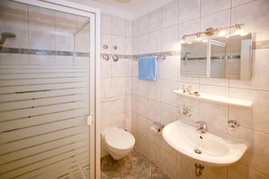 A bathroom with a glass shower door, a toilet, a sink with a mirror above it, and a towel hanging on the wall. - (22) 2-room apartment - apartment house Sonnenresidenz I (Kühlungsborn)