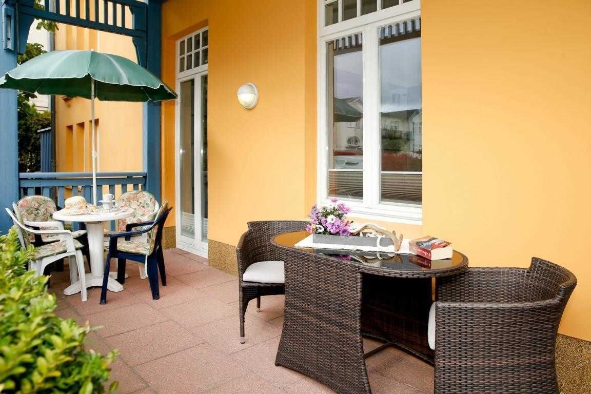 An outdoor patio with wicker furniture, a table with a vase of flowers, and a blue umbrella.