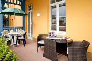 An outdoor patio with wicker furniture, a table with a vase of flowers, and a blue umbrella. - (22) 2-room apartment - apartment house Sonnenresidenz I (Kühlungsborn)