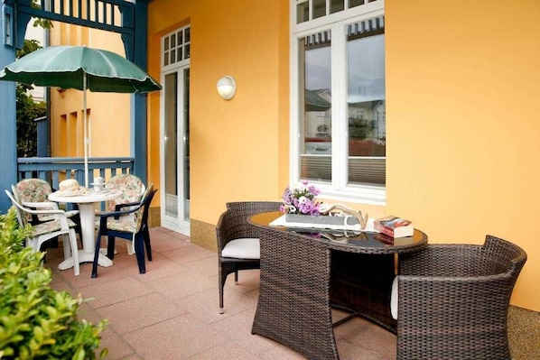 An outdoor patio with wicker furniture, a table with a vase of flowers, and a blue umbrella. - (22) 2-room apartment - apartment house Sonnenresidenz I (Kühlungsborn)