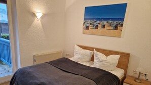 Ein Schlafzimmer mit einem Bett, einem Nachttisch, einer Wandlampe und einem Gemälde mit einer Strandansicht.