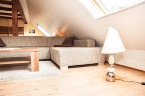 A cozy loft bedroom with a sloped ceiling, a sofa, a small table, and a lamp.