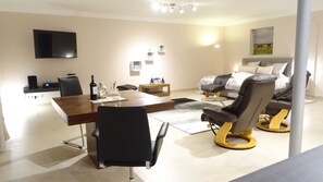 A modern living room with a dining area, a sofa set, a massage chair, and a flat-screen TV.