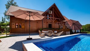 Een houten hut met een zwembad, buitenzitplaatsen en parasols.
