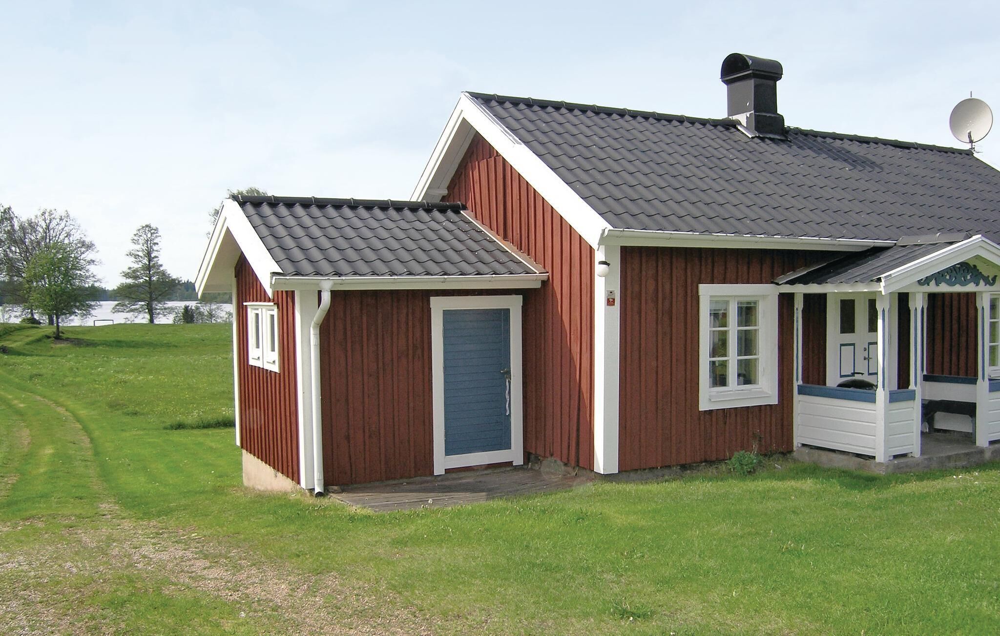 A red wooden house with a grey roof, a satellite dish, and a small porch with white trim.