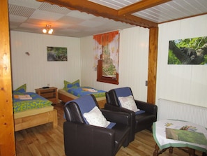 A room with two beds, a wooden-framed ceiling, a window with a view of trees, and a table with a tablecloth.