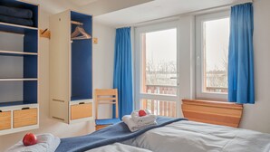 Un dormitorio con cama, armario, silla y ventana con cortinas.