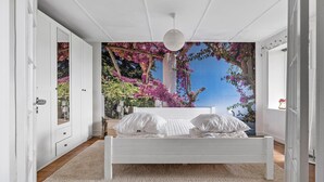 Une chambre avec un lit blanc, une grande fresque représentant des fleurs roses et un plafond blanc.