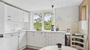 Une cuisine moderne avec des meubles blancs, un lave-vaisselle Bosch, une machine à café et une vue sur la verdure environnante.