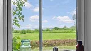 Une fenêtre donnant sur un champ verdoyant et une étendue d’eau.