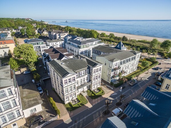 A residential area with a large building featuring a central courtyard, a beach in the background, and a pier extending into the water.