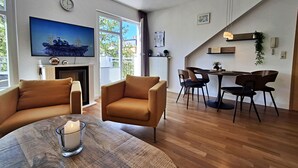 Ein Wohnzimmer mit Kamin, einer Essecke mit Tisch und Stühlen, einem an der Wand befestigten Fernseher und einem großen Fenster.