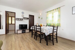 Een eetruimte met een tafel voor vier personen, een televisie en een deur naar een andere kamer.