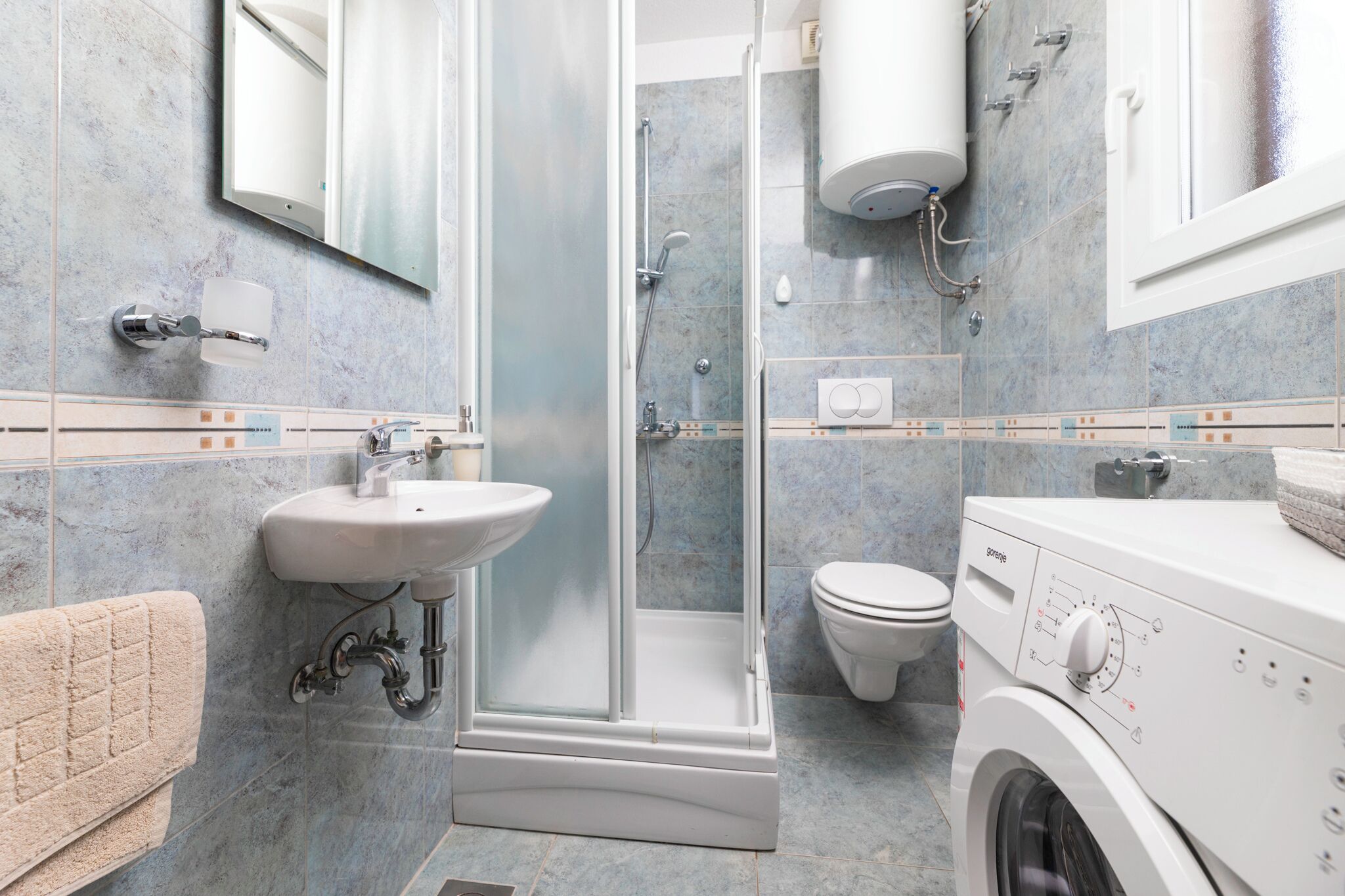 A modern bathroom with a glass-enclosed shower, a sink, a toilet, and a washing machine.