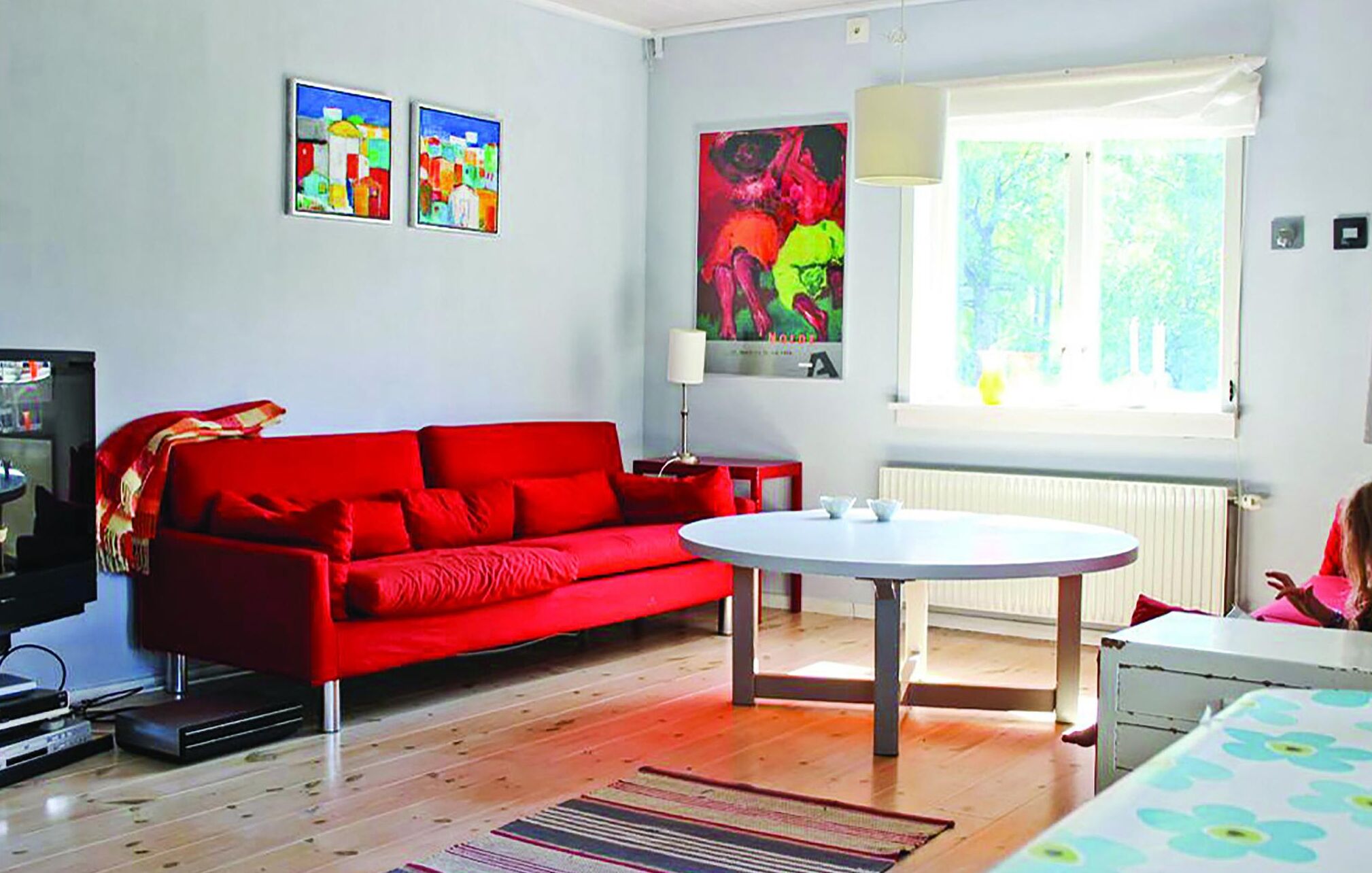 Une pièce avec un canapé rouge, une table ronde et une fenêtre donnant sur un paysage verdoyant.
