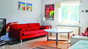 Una habitación con un sofá rojo, una mesa redonda y una ventana con vistas a follaje.