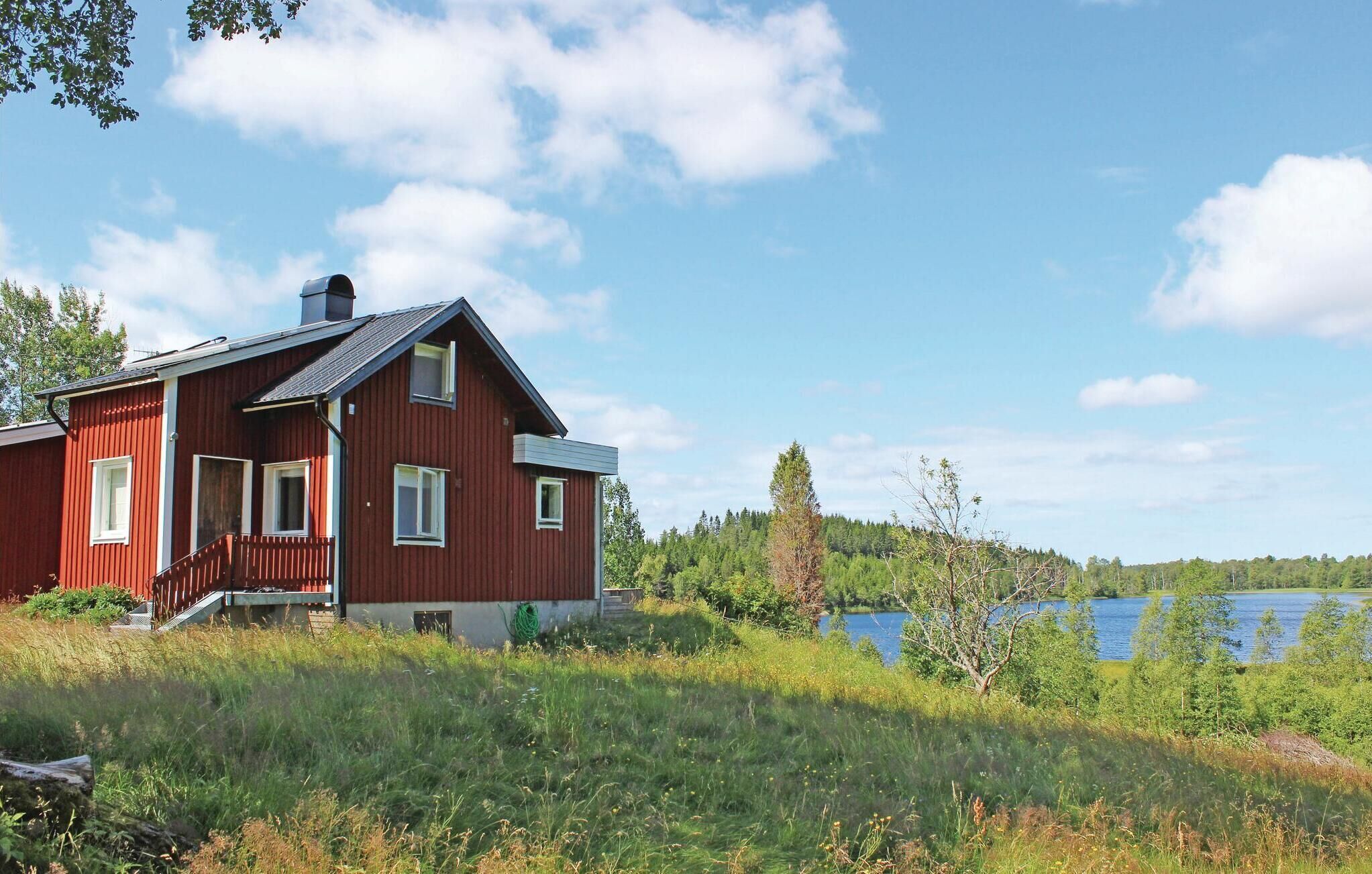 Une maison en bois rouge, dotée d’un balcon, entourée d’une végétation luxuriante et bordée d’un lac.