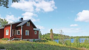 Una casa de madera roja con balcón, rodeada de exuberante vegetación y un lago.