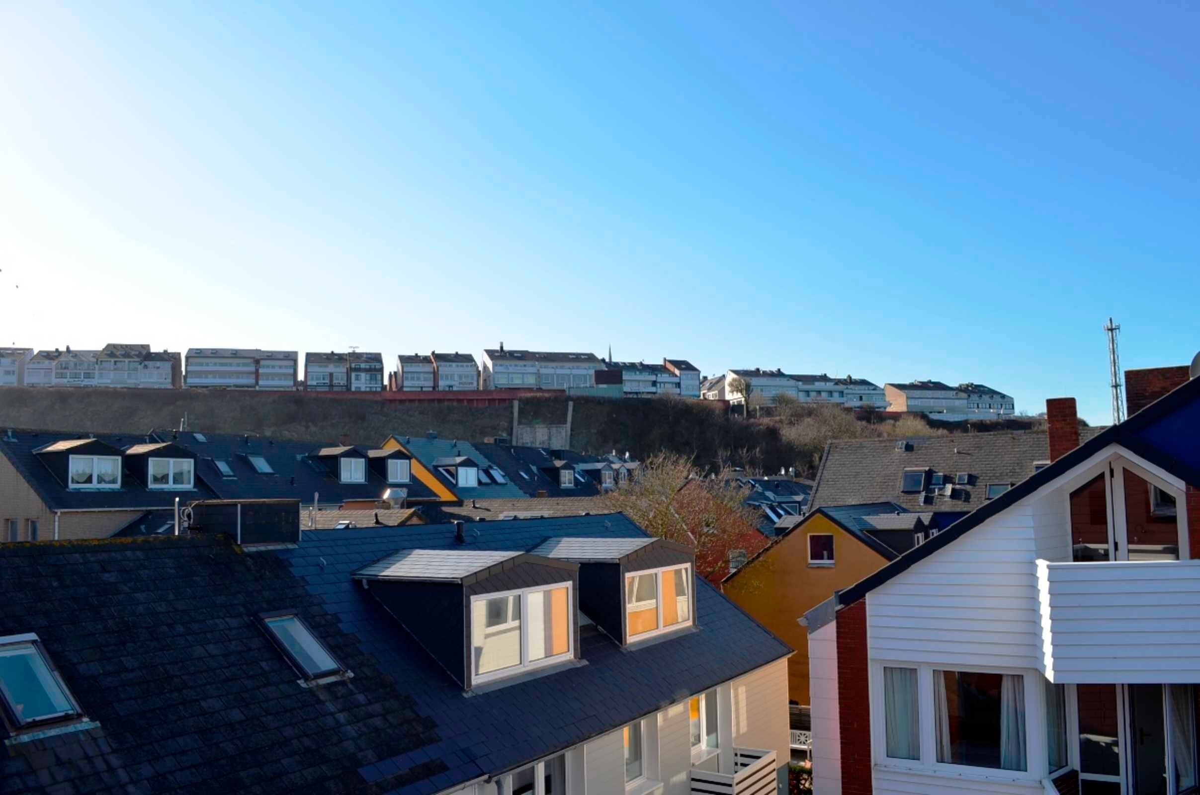 A residential area with multiple houses, some with sloped roofs and others with flat roofs, under a clear sky.