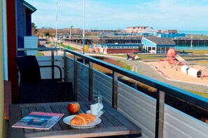 A balcony with a table, a chair, a magazine, a plate with food, and a drink. - Sino Suite, 2. OG, balcony seafront, - Dünenblick Apartments (Helgoland)