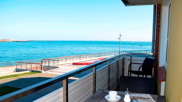 A balcony with a view of the sea, a table with a newspaper, and a chair. - Sino Suite, 2. OG, balcony seafront, - Dünenblick Apartments (Helgoland)