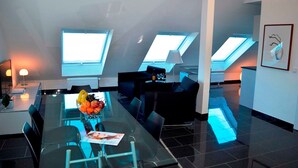A modern living room with a glass dining table, black sofas, and a fruit bowl. - Sino Suite, 2. OG, balcony seafront, - Dünenblick Apartments (Helgoland)