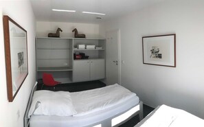 A small, neatly organized room with a bed, a red chair, a wardrobe, and a framed picture on the wall. - Sino Suite, 2. OG, balcony seafront, - Dünenblick Apartments (Helgoland)