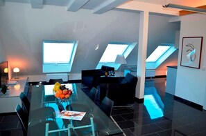 A modern living room with a glass dining table, black sofas, and a fruit bowl. - Sino Suite, 2. OG, balcony seafront, - Dünenblick Apartments (Helgoland)
