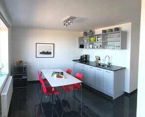 A modern kitchen with a white countertop, red chairs, a sink, and a microwave. - Sino Suite, 2. OG, balcony seafront, - Dünenblick Apartments (Helgoland)