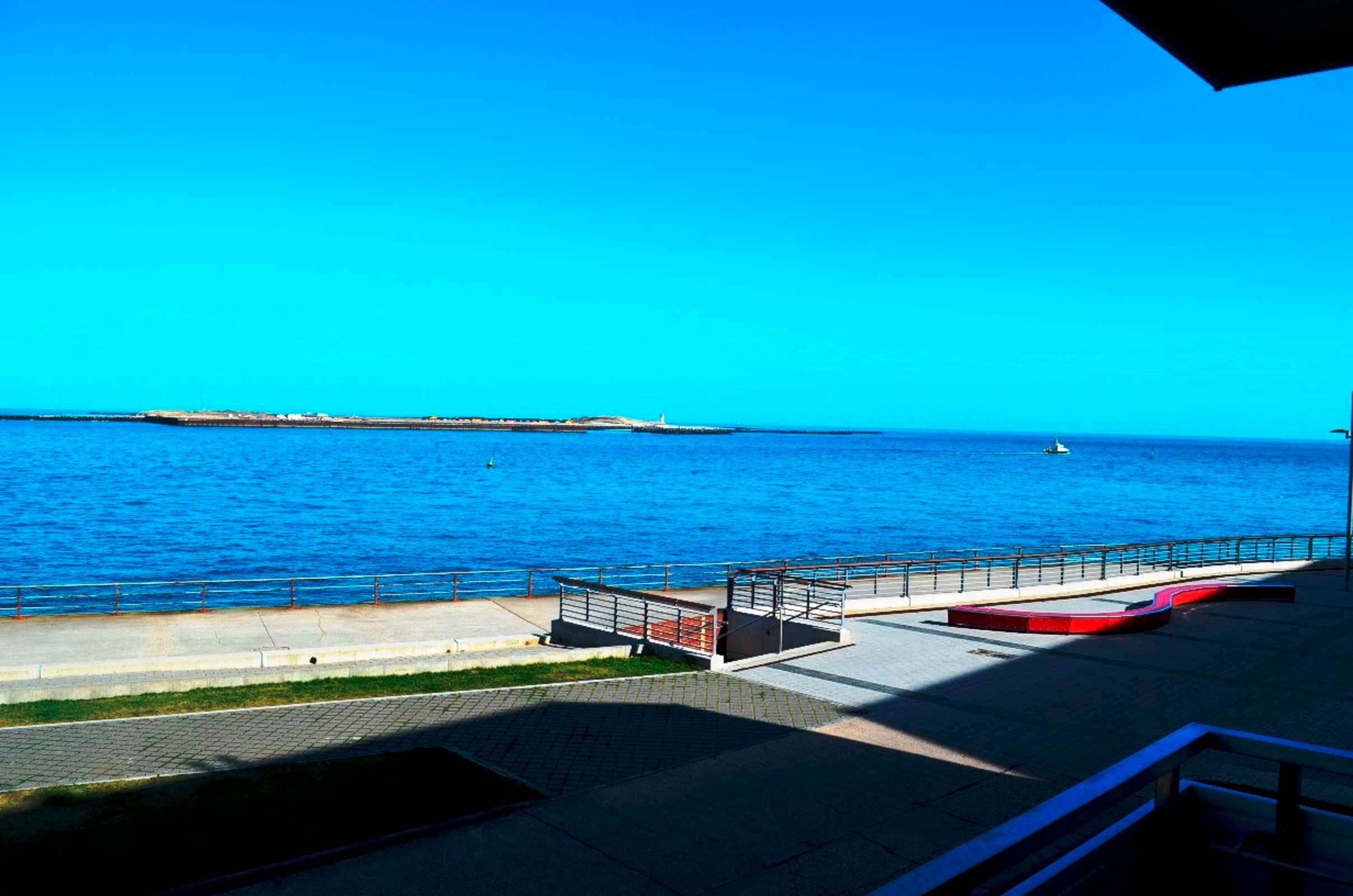 A coastal walkway with a railing, a bench, and a distant shoreline.