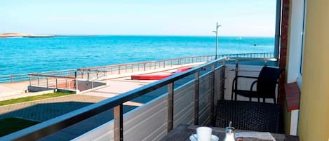 Een balkon met uitzicht op zee, een tafel met een krant en een stoel.