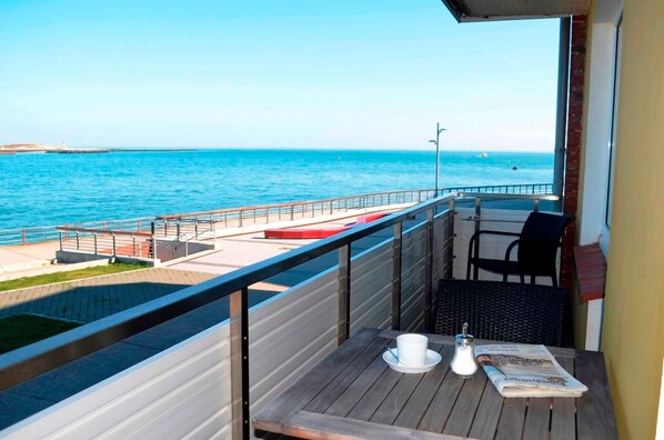 A balcony with a view of the sea, a table with a newspaper, and a chair. - Sino Suite, 2. OG, balcony seafront, - Dünenblick Apartments (Helgoland)