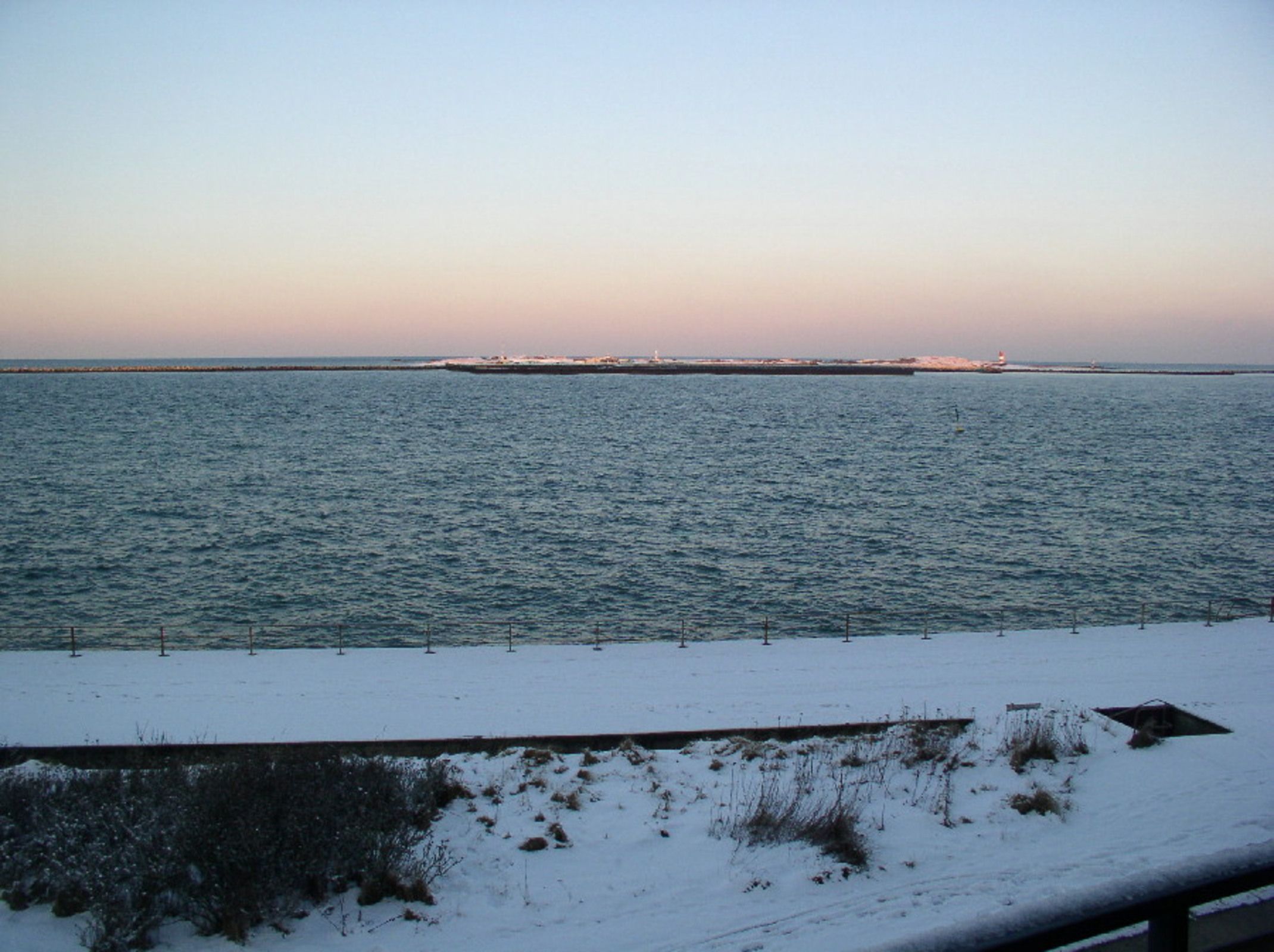A snowy landscape with a body of water and a distant shoreline.