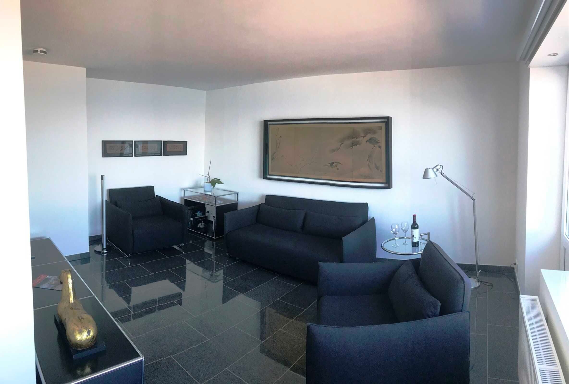 A modern living room with a black sofa, a small coffee table, a floor lamp, and a painting on the wall.