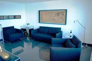 A modern living room with a blue sofa set, a glass coffee table, and a framed artwork on the wall. - Sino Suite, 2. OG, balcony seafront, - Dünenblick Apartments (Helgoland)