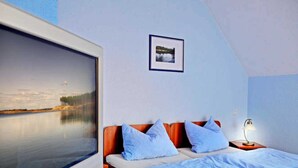 A bedroom with a large window, a bed with blue pillows, a nightstand with a lamp, and a framed picture on the wall. - Vacation apartment 1 - 55 sqm (2-4 persons), balcony - Weichaer Hof FBS Sonja Fritsch (Weißenberg)