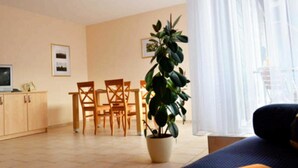 A living room with a sofa, a dining table with chairs, a potted plant, and a TV on a cabinet. - Vacation apartment 1 - 55 sqm (2-4 persons), balcony - Weichaer Hof FBS Sonja Fritsch (Weißenberg)