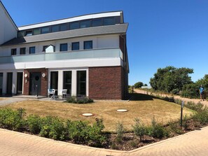 A modern two-story building with a brick facade, large windows, and a paved entrance area with outdoor seating.