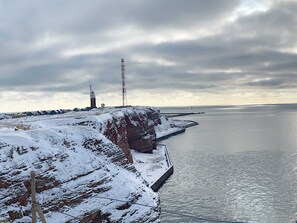 Paisaje costero con un acantilado cubierto de nieve, un faro y un mar tranquilo bajo un cielo nublado.