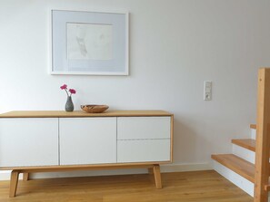 A minimalist room with a wooden bench, a white cabinet, a framed artwork, and a vase with flowers. - Apartment 08 - gate to the sea (Helgoland)