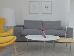 A living room with a grey sofa, a yellow armchair, a white coffee table with flowers, and a small table with a candle.