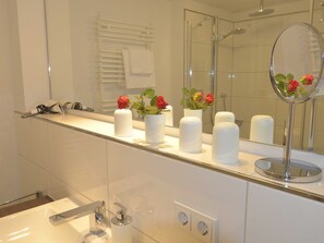 Een moderne badkamer met een douchecabine van glas, een wastafel met spiegel en toiletartikelen op het aanrecht.