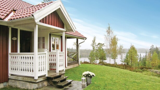 Ein Haus mit Veranda, einem kleinen Garten und Blick auf einen See.