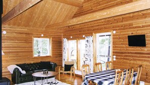 Ein gemütliches Blockhaus-Interieur mit Holzausbau, einem Esstisch mit Stühlen, einer Couch und einem kleinen runden Tisch.