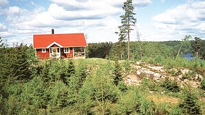 Ein rotes Haus mit Veranda, umgeben von dichtem Grünwald und einem See im Hintergrund.