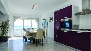 Una cuina moderna amb armaris de color morat, un forn de mur i una zona de menjador amb vista al mar.